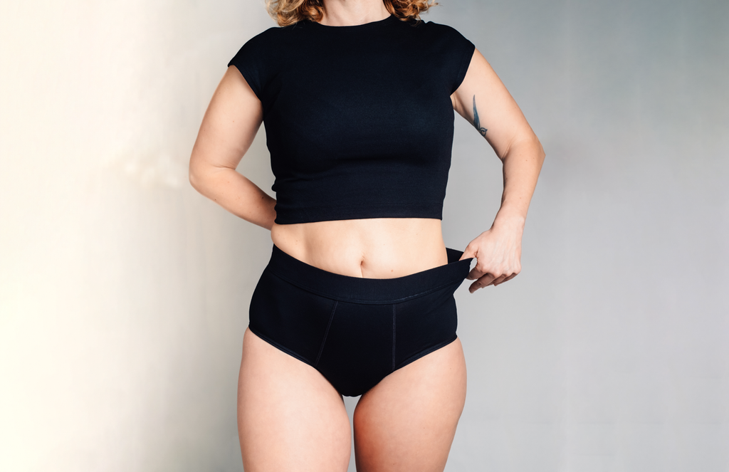 L'Indispensable portée de face. La culotte menstruelle noire, large élastique à la taille, confortable pour flux très abondant et retour de couche.